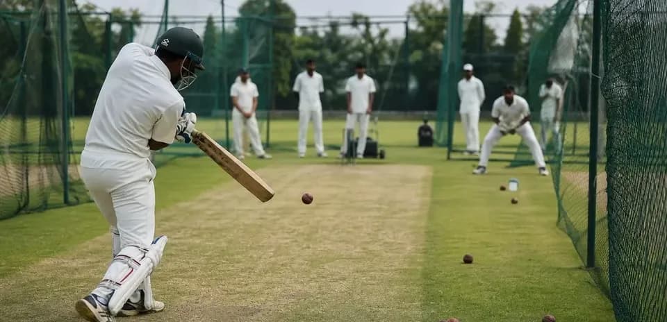 Batsman practicing in cricket nets with teammates observing