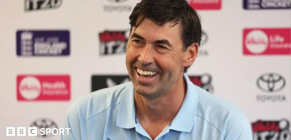 Cricket coach smiling at press conference backdrop