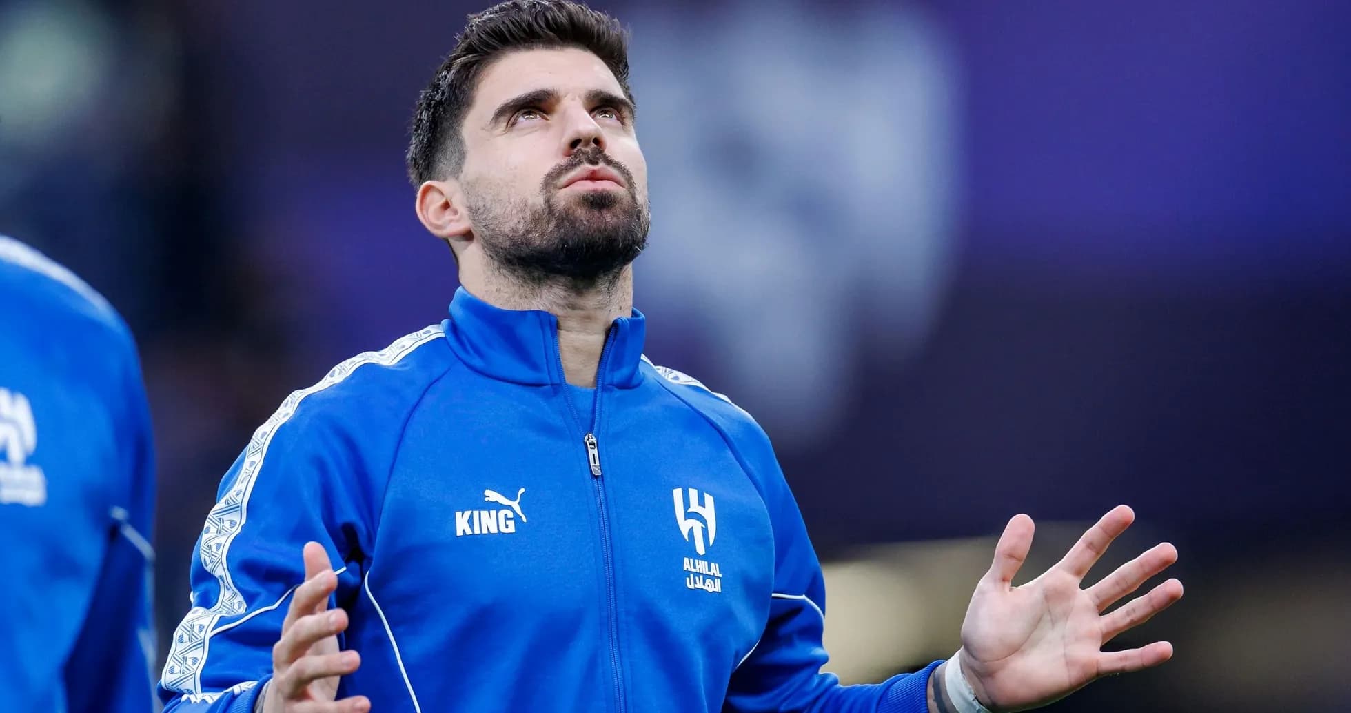Player in blue jacket looking up before match