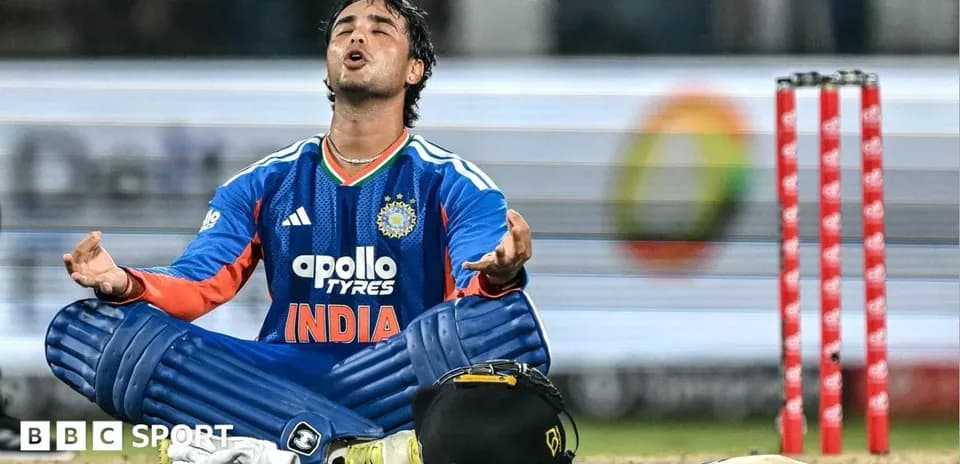 Cricketer seated on field, arms raised in prayer