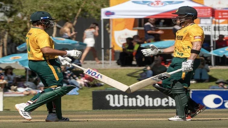 Two cricketers celebrating with bats on the field