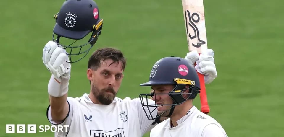 Two cricketers celebrating a milestone with helmets raised