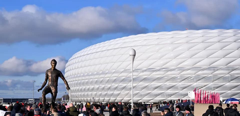 Crowd gathering outside stadium with statue