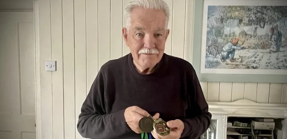 Elderly man holding medals in a home setting