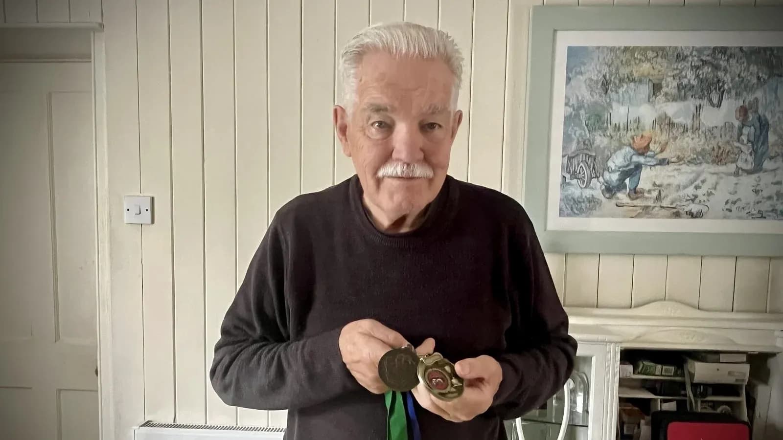 Elderly man holding medals in a home setting