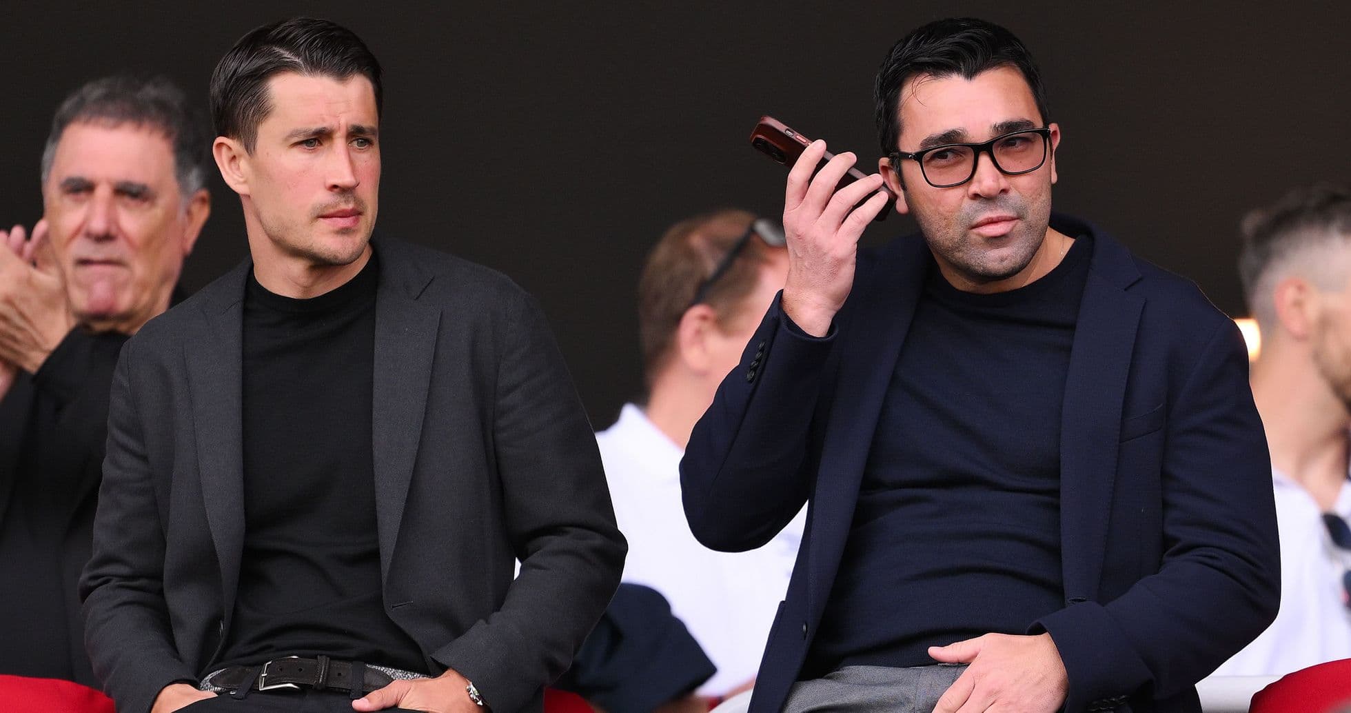 Two men seated, one using a mobile device