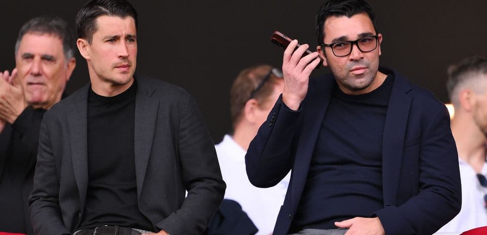 Two men seated, one using a mobile device