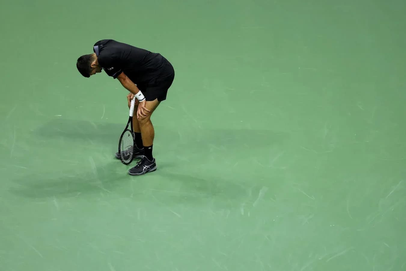 Tennis player bending over holding racket on court