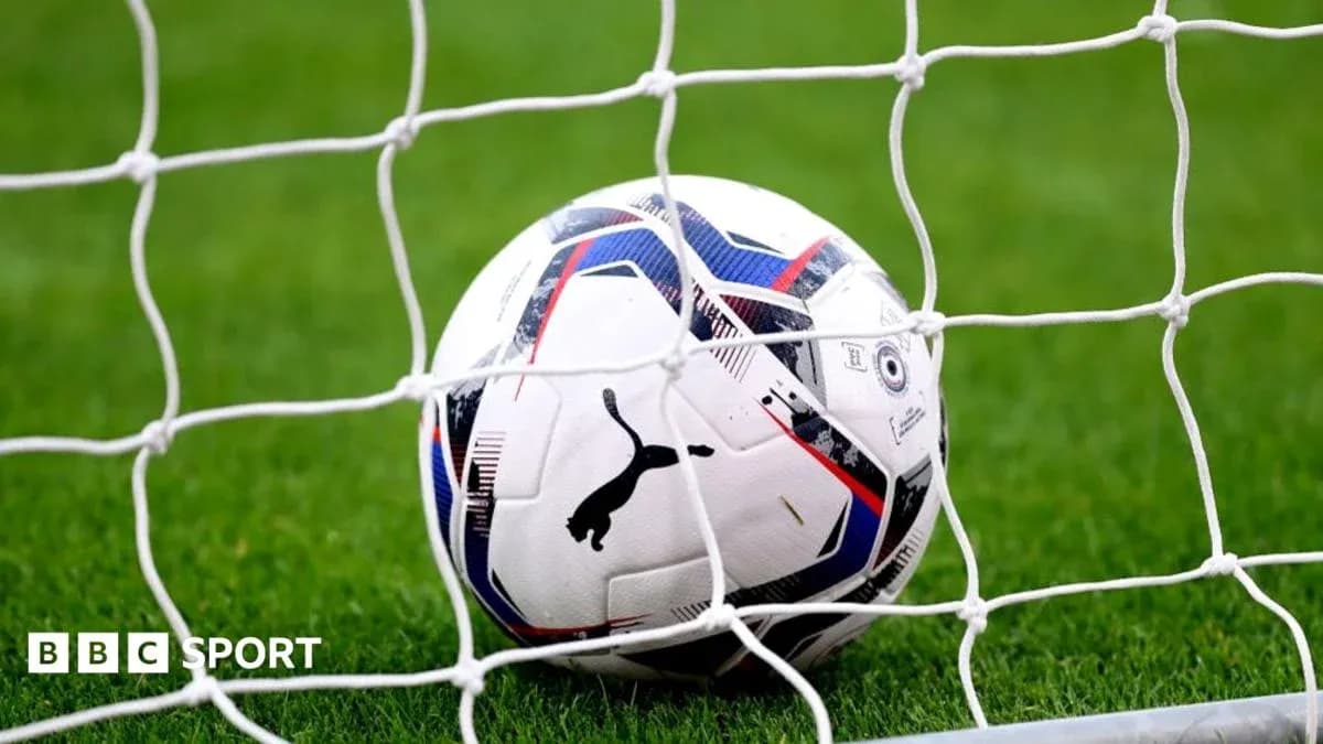 Football resting in the goal net on grass