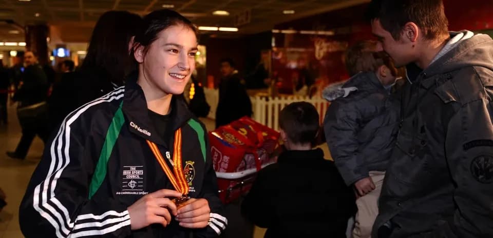 Athlete holding medal in airport, smiling at companion