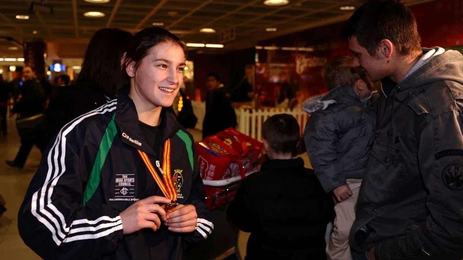 Athlete holding medal in airport, smiling at companion