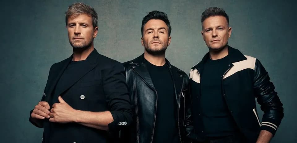 Three men posing in stylish outfits against backdrop