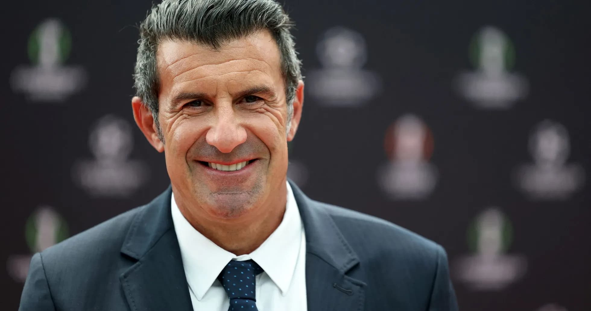 Man in a suit smiling at event backdrop Man in a suit smiling at event backdrop
