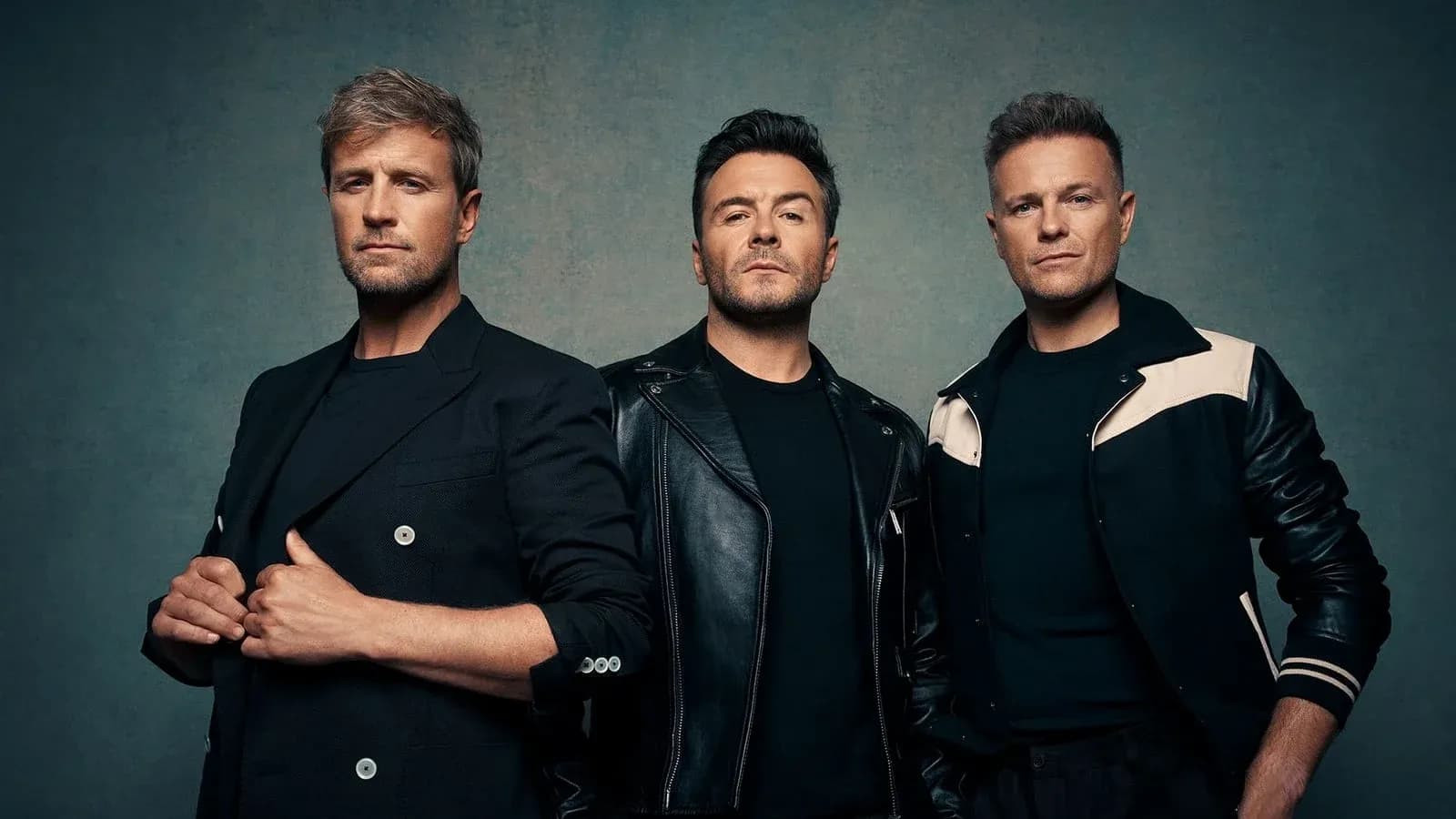 Three men posing in stylish outfits against backdrop Three men posing in stylish outfits against backdrop